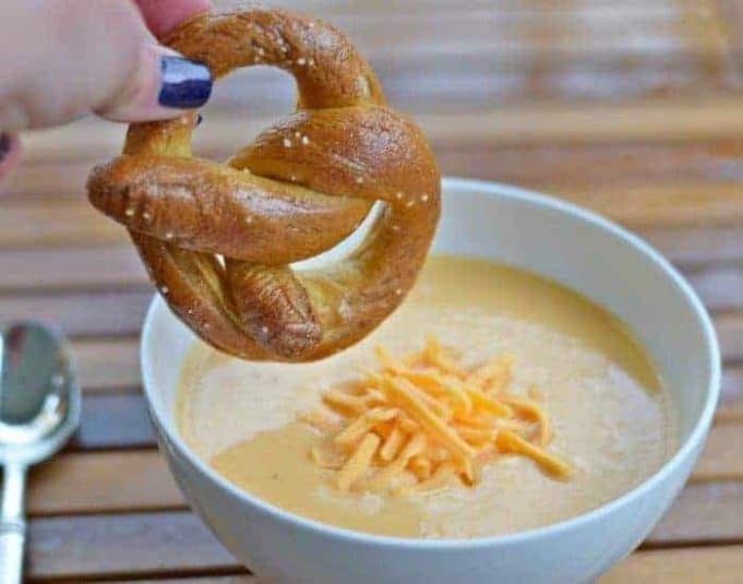 Image shows Pretzel dipping into beer cheese soup.