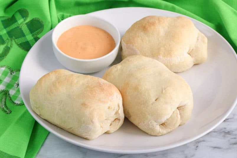 Reuben rolls made with pizza dough on a white plate with a small bowl of thousand island dressing.