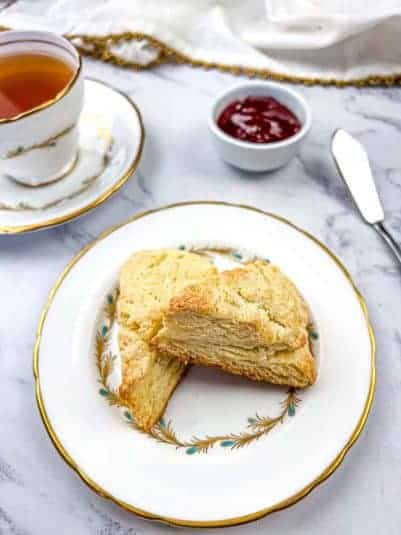 Two butter scones on a plate with a cup of tea on a marble surface.