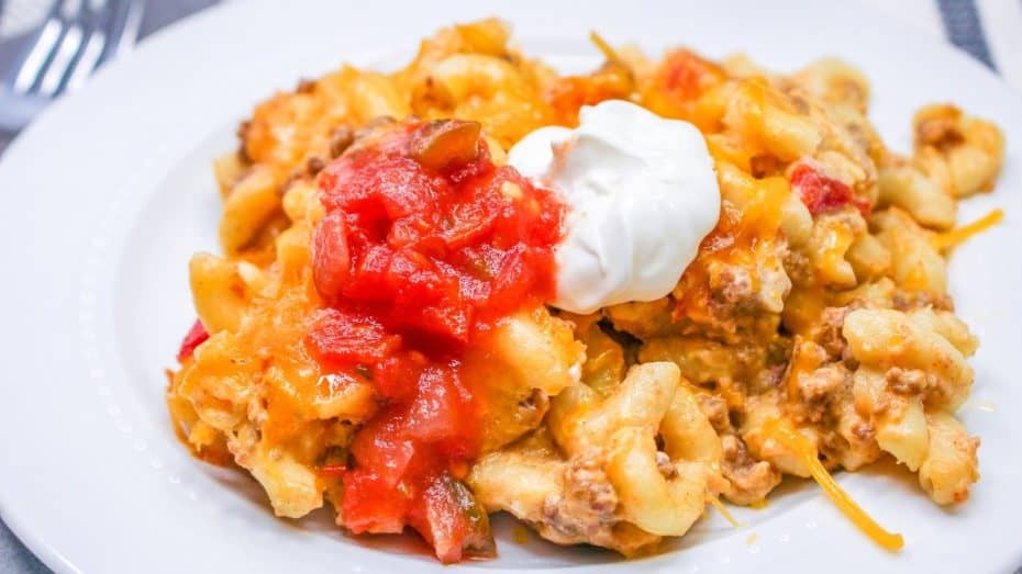 A plate of cheesy pasta with ground meat, topped with tomato sauce and a dollop of sour cream.