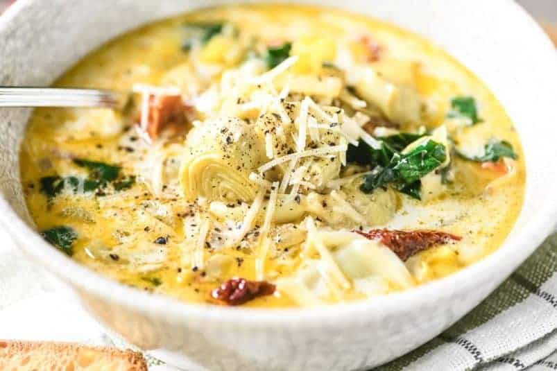 Tuscan artichoke soup in a bowl with chredded cheese.