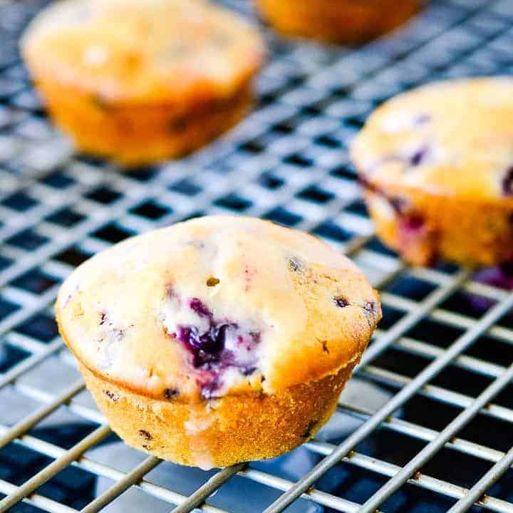 Blackberry muffins drizzled with lemon glaze sitting on a gray cooling rack on a dark background.