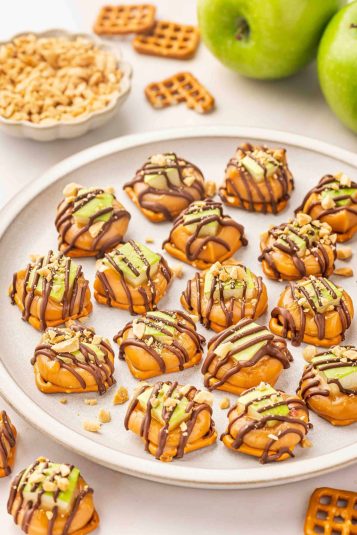 Caramel apple pretzel bites on a white plate with a sprinkle of crushed peanuts.