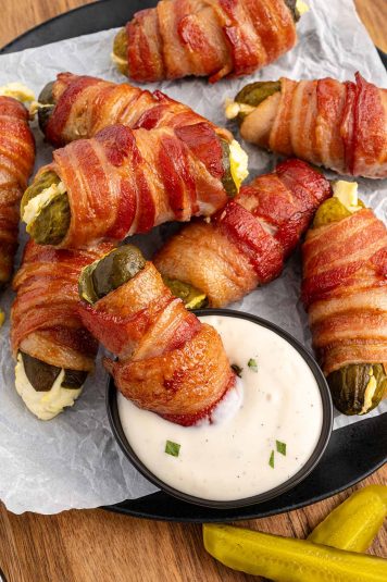 A plate of Bacon Wrapped Pickles with a side of ranch dipping sauce.