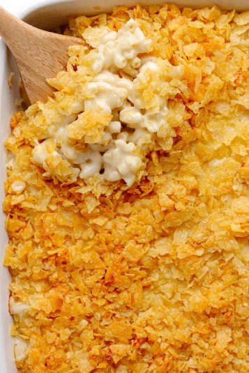 Wooden spoon lifting out some baked white cheddar mac and cheese with chip topping.