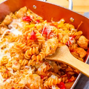 Creamy baked pasta with chicken, cheese, and red peppers in a casserole dish.