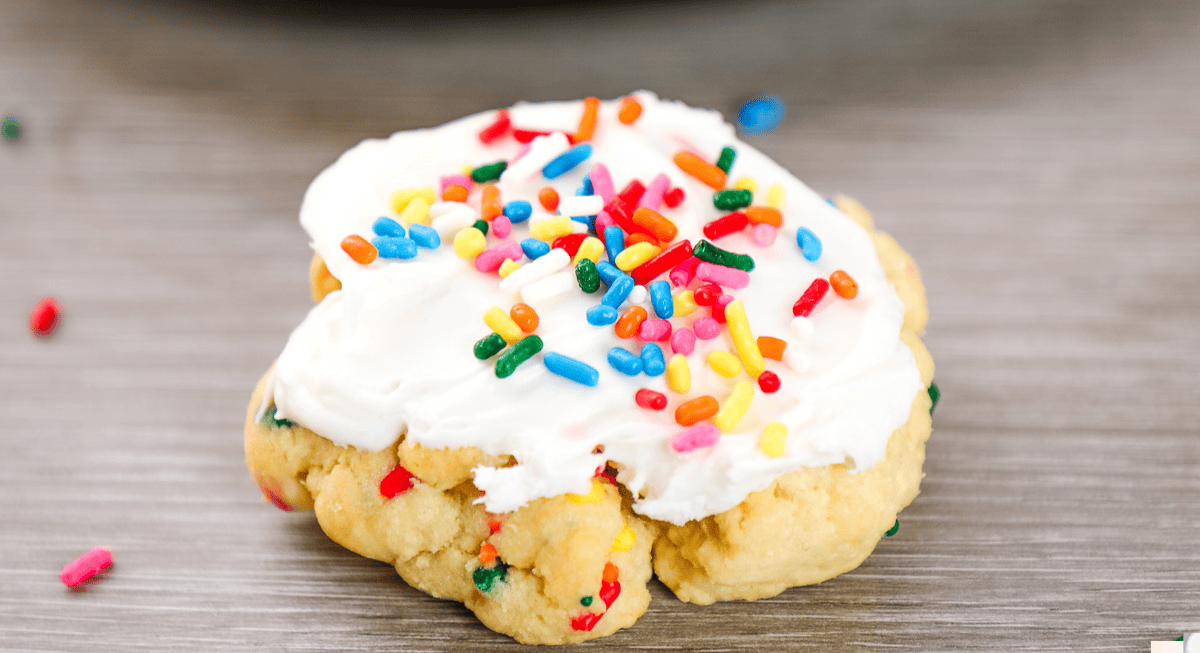 a frosted birthday cake cookie topped with icing and rainbow sprinkles.