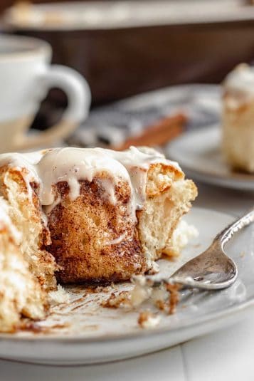 A cinnamon roll on a plate with a fork and bites removed.