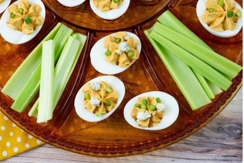 Buffalo deviled eggs garnished with blue cheese and green onions on a serving tray.