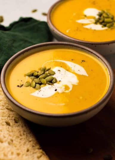 Curried squash soup in a shallow, ceramic bowl, topped with pumpkin seeds and creme fraiche.