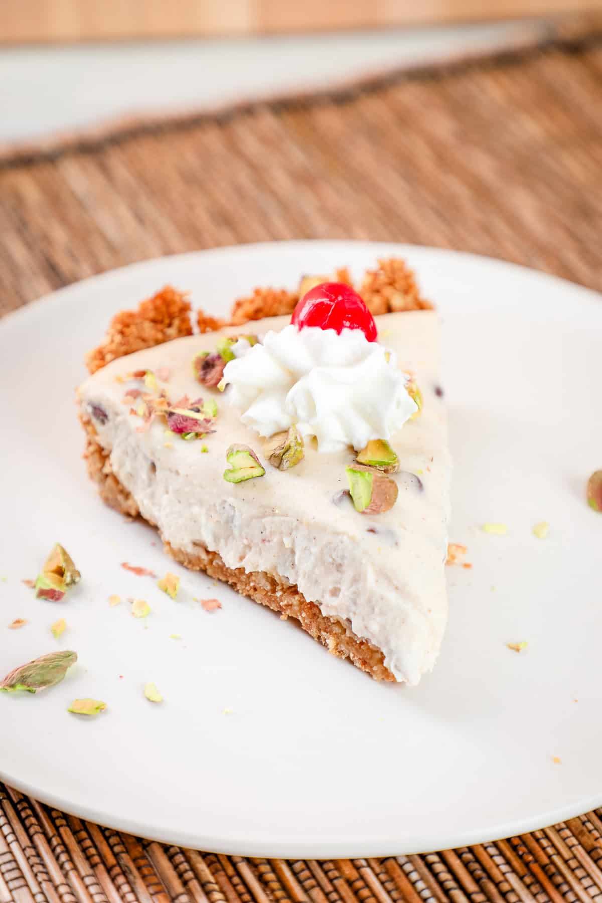 a slice of cannoli pie with chocolate chips topped with pistachios, whipped cream, and a marachino cherry.