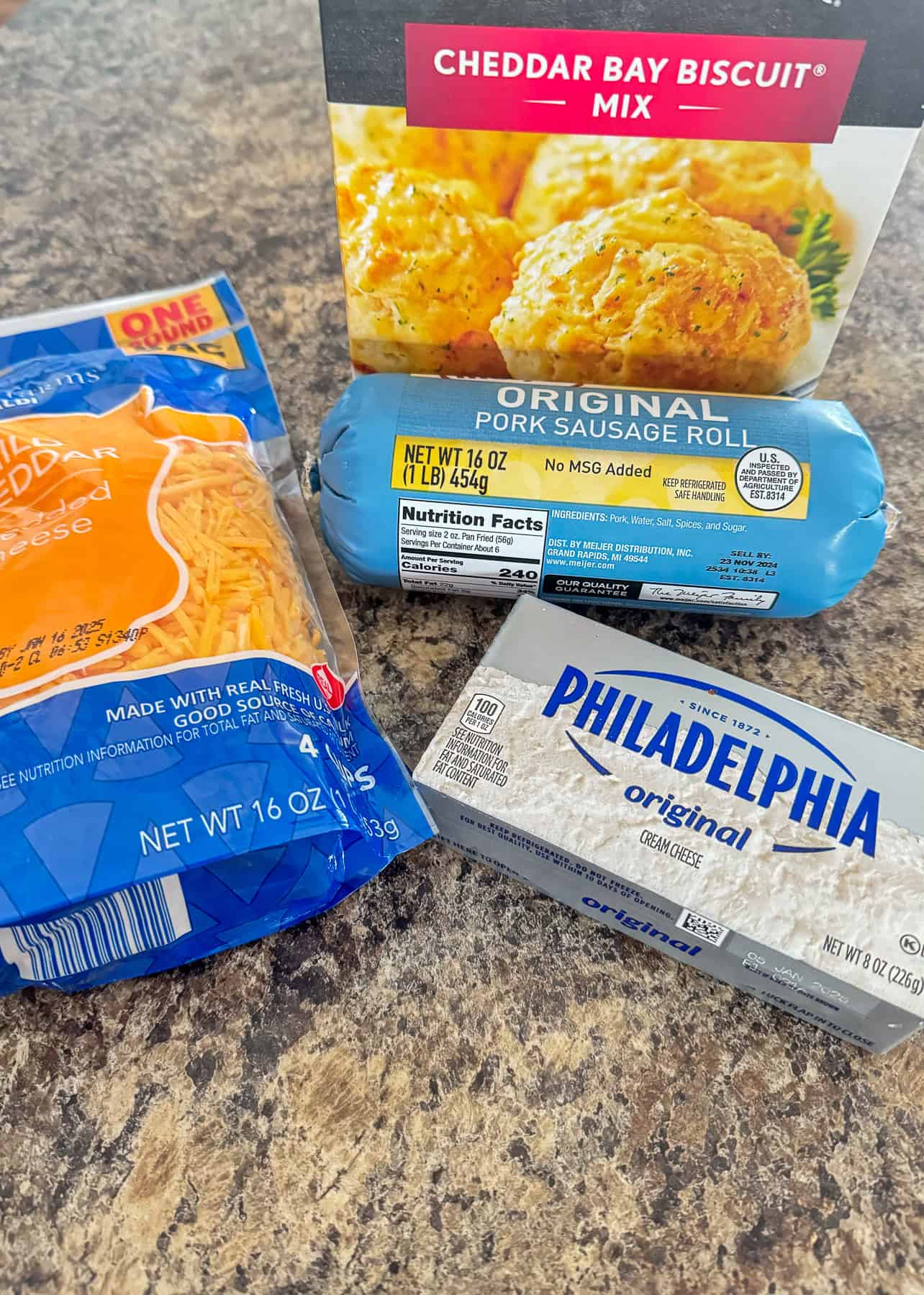 Cheddar Bay biscuits, pork sausage rolls, shredded cheese, and cream cheese on a kitchen counter.