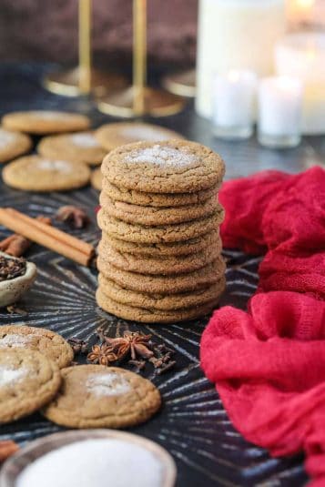 Chewy spiced molasses cookies stacked on a black surface.