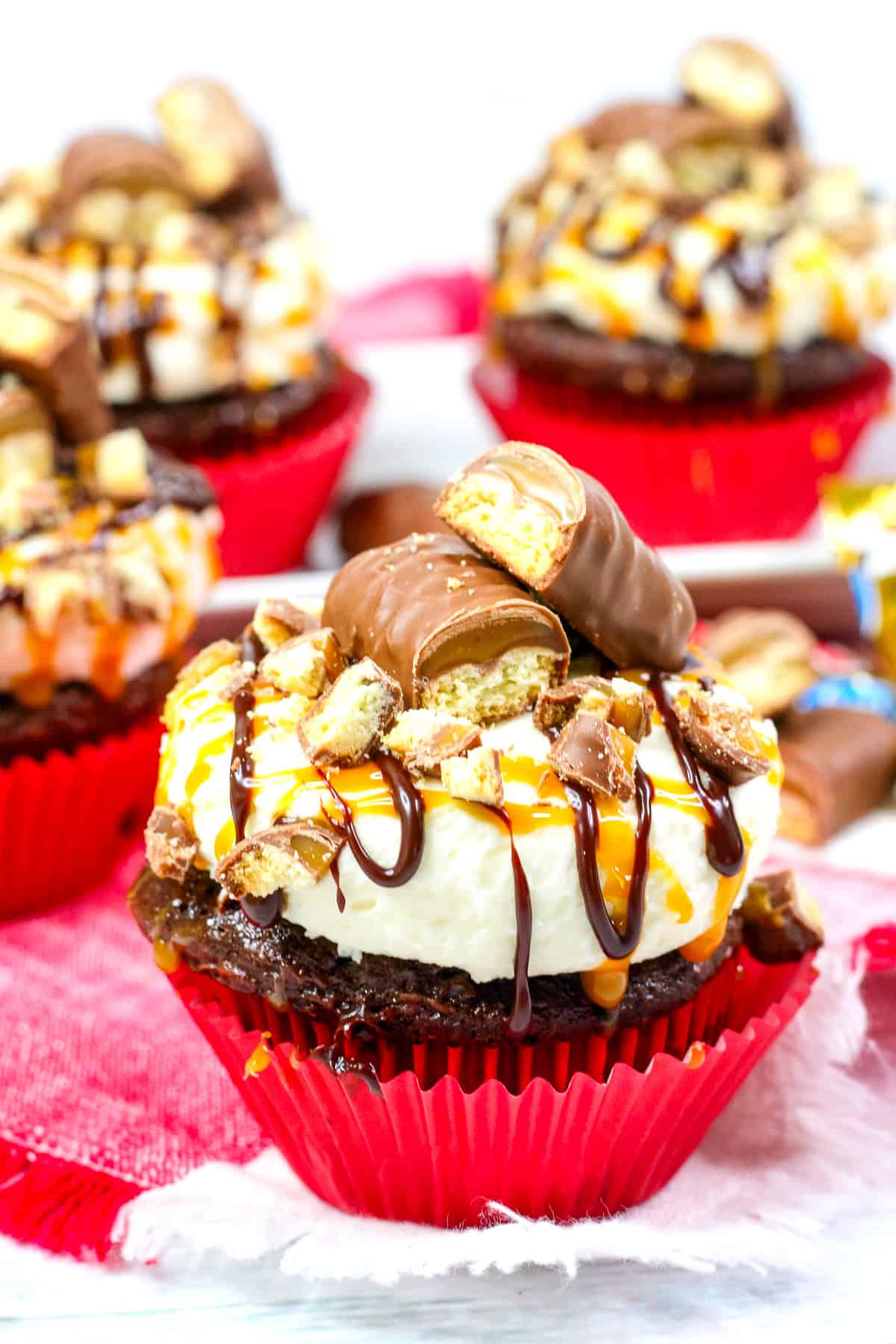 chocolate cupcakes topped with caramel buttercream, caramel sauce, and a cut in half Twix bar.