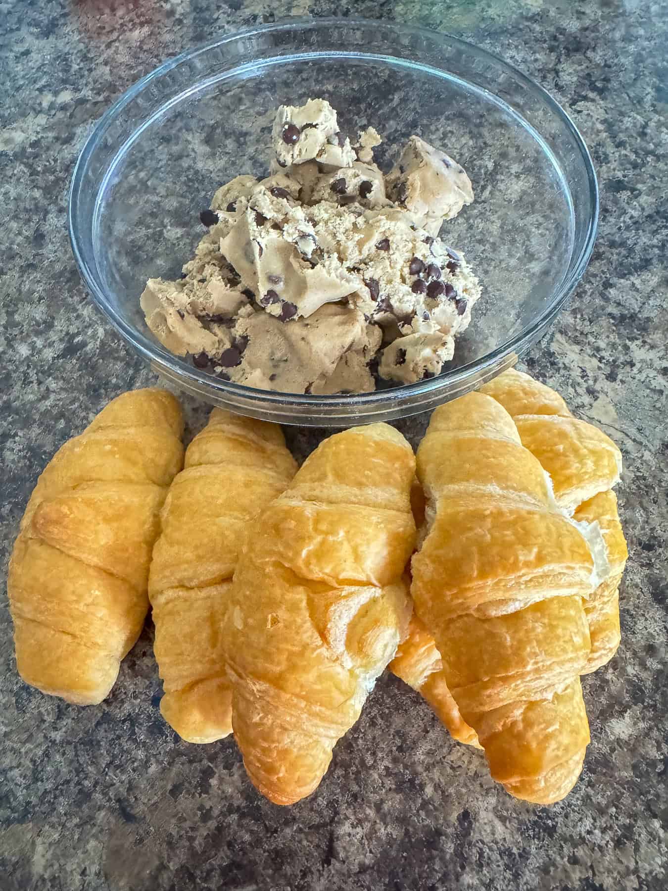 6 croissants and a bowl of chocolate chip cookie dough on a kitchen counter.