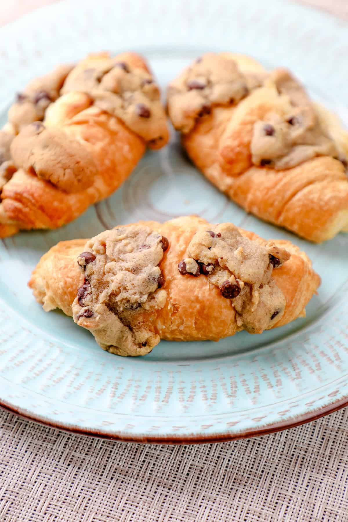 three cookie dough croissants topped with more chocolate chip cookie dough on a plate. 