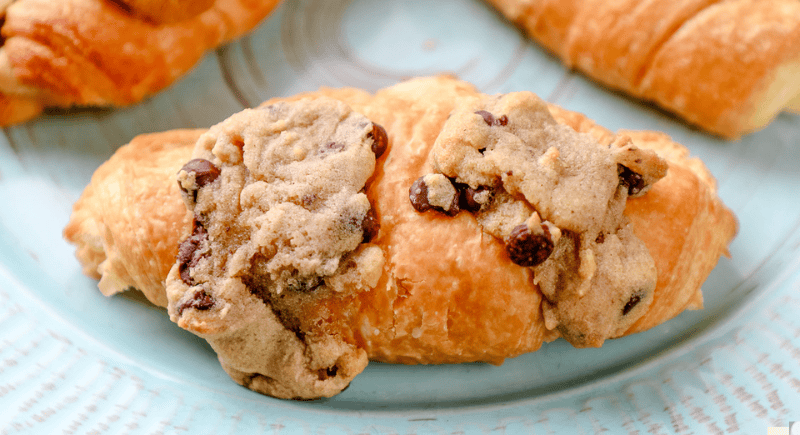 Three cookie dough croissants topped with more chocolate chip cookie dough on a plate.