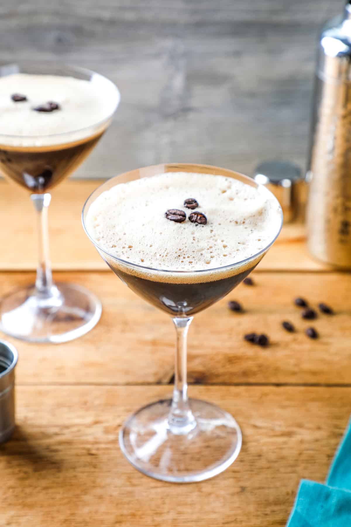 a creamy espresso martini with a foamy top topped with 3 coffee beans in a martini glass. 