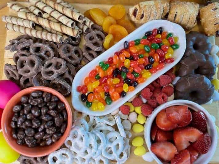 Easter candy charcuterie on a wooden board with plates and glasses in background.