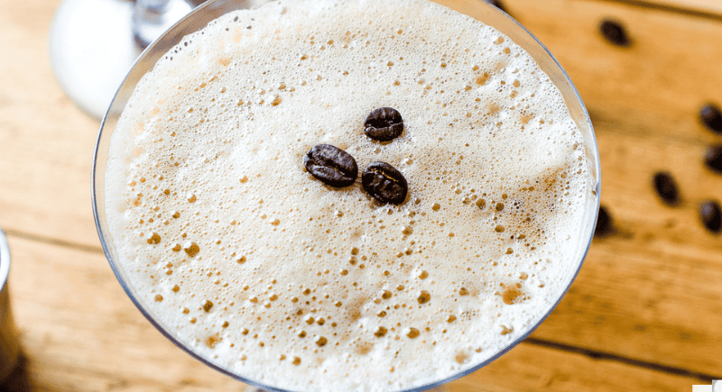 a closeup of an foamy creamy espresso martini garnished with 3 coffee beans.
