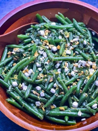Green bean salad with goat cheese, lemon zest, pistachios, and fresh basil in a wooden salad bowl.