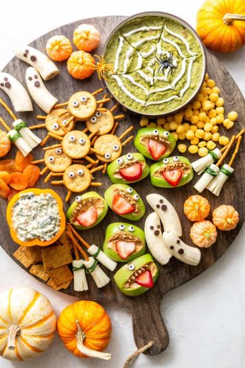 Healthy Halloween Snack Board with Spider Web Guacamole, Boo-Nanas, Clementine Pumpkins, Witches Brooms, Apple Monsters and Spider crackers.