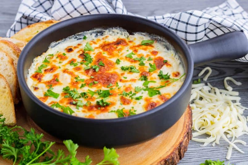 A cheesy golden baked Shrimp scampi dip in a black baking dish.