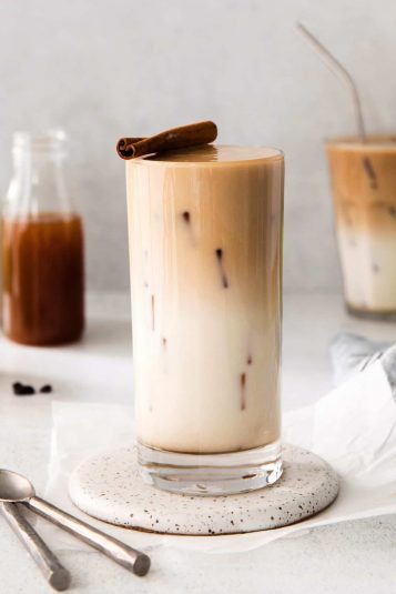 Iced apple crisp macchiato in glass topped with cinnamon stick.