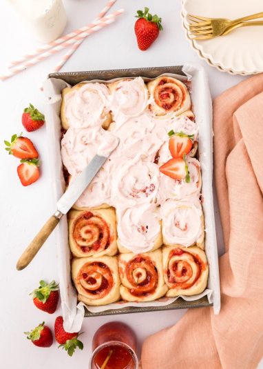 Frosting strawberry cinnamon rolls.