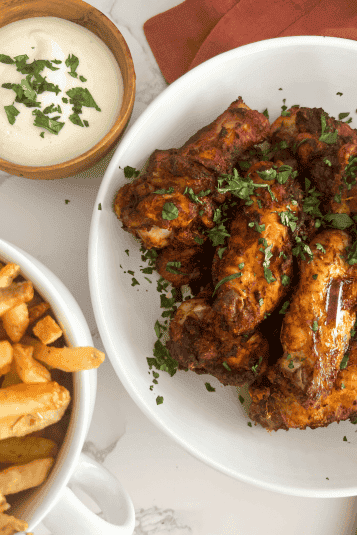 Tandoori chicken wings on a plate with cilantro as a garnish with fries and ranch next to it.