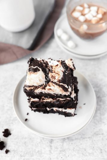 Angled overhead photo of 3 hot cocoa brownies on round white plates with a cup of hot cocoa in the background.