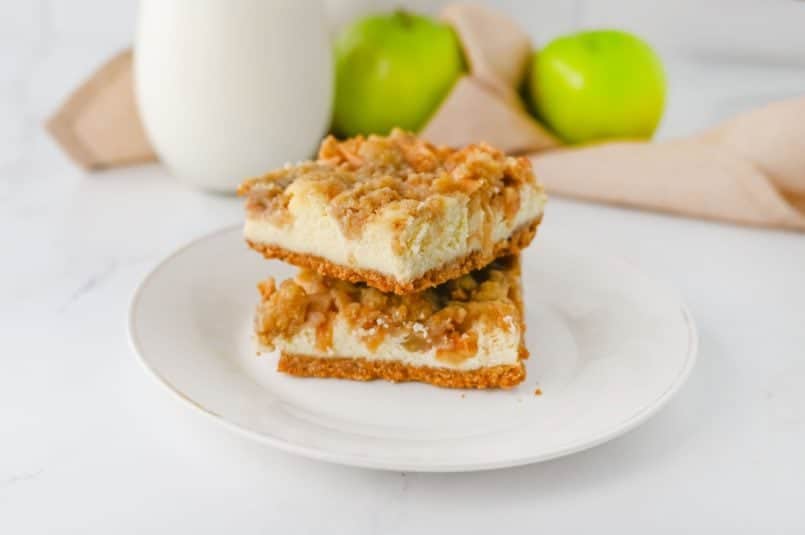 cream cinnamon apple cheesecake bars stacked on a white plate with a glass of milk.