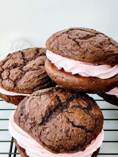Indulge in chocolate cookies with pink frosting, resembling soft, cake-like treats filled with creamy strawberry buttercream.