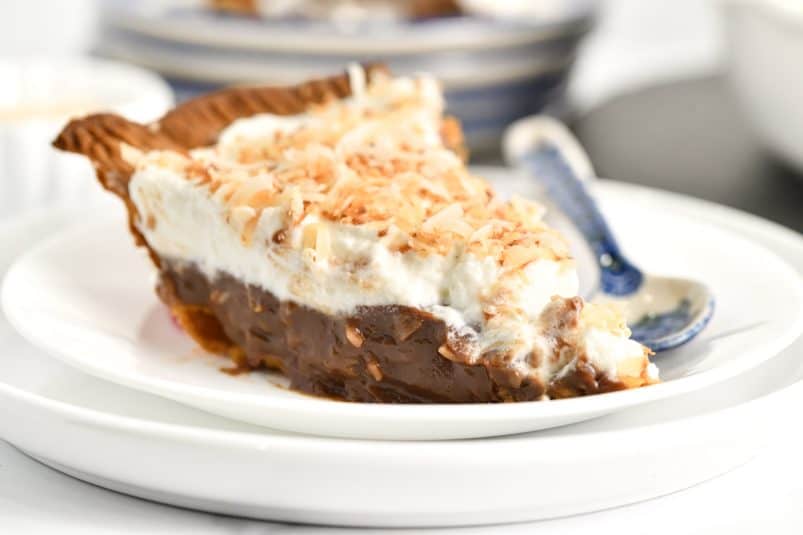 Slice of chocolate coconut cream pie on a white plate with a blue polish pottery dessert spoon.