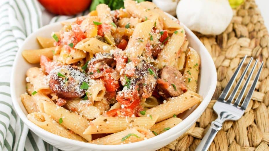 A baking dish filled with creamy pasta topped with a golden breadcrumb crust. A spoon is serving a portion.