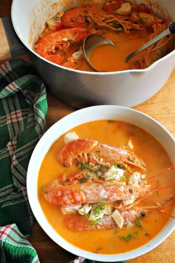 A white bowl with fish and prawns stew, a pot of stew, and a green tea towel around them.