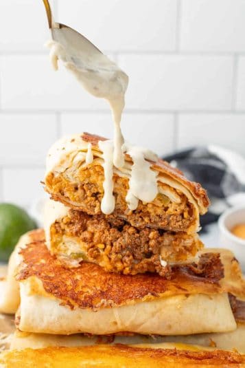 grilled cheese burrito cut in half and stacked with queso being spooned over the top