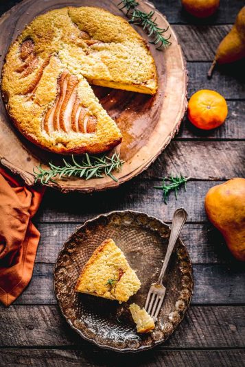 A tables cape with an Italian ricotta cake with pears on a wood board with a slice cut out and set on a small plate.