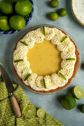 Key lime pie on a green tea towel surrounded by whole and cut limes.
