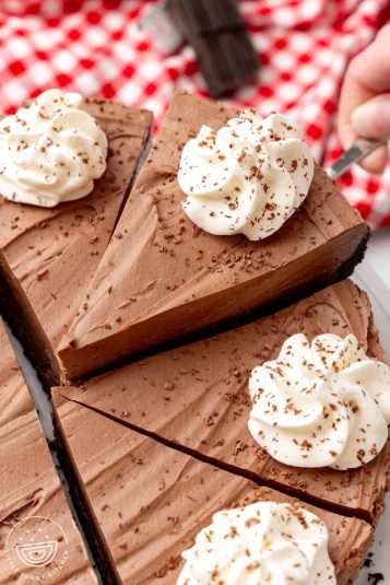 A no bake chocolate cheesecake cut into slices. One slice is being lifted up with a cake server.