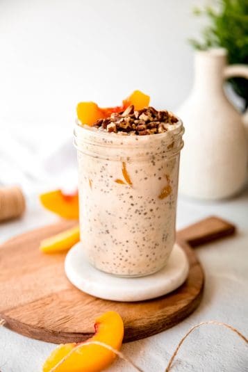 Clear mason jar filled with a serving of high protein peach overnight oats topped with chopped pecans and fresh peach slices.