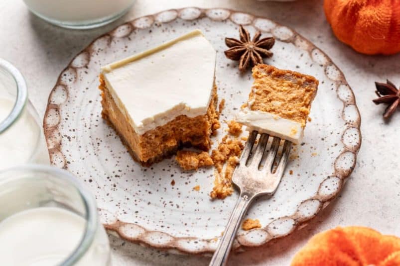 A fork holding a bite from a pumpkin cheesecake bar on a plate.