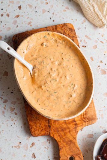 A bowl of creamy chipotle sauce on a small wooden cutting board set on a counter.