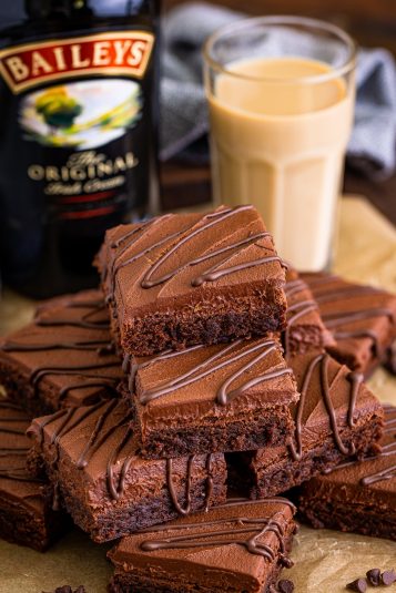 Bailey's Brownies stacked on brown parchment paper, a glass of Irish Cream and alcohol bottle in the background.