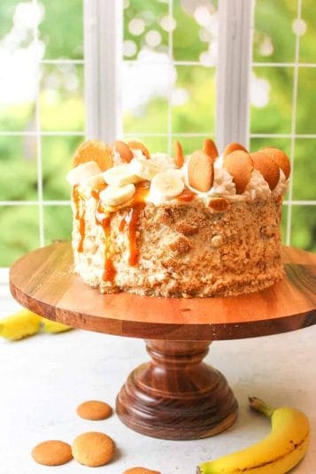Southern banana pudding cake fully decorated and sitting on a wooden cake stand.