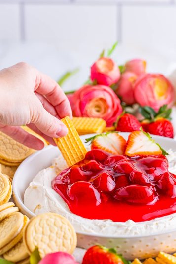 A hand dipping a cookie into Cheesecake Dip.