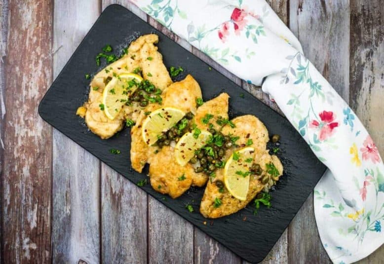 Two chicken piccata on a white plate with parsley and lemon wedges.