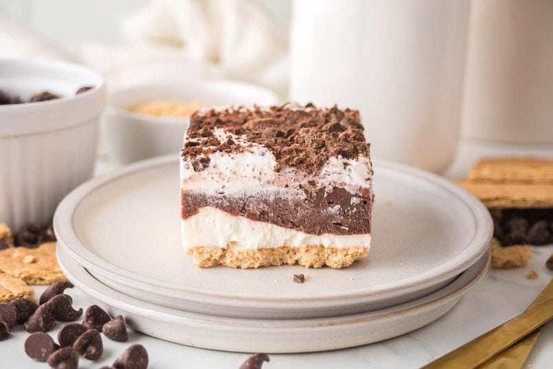 A chocolate delight awaits on the plate, boasting a graham cracker crust, a creamy white layer, a luscious chocolate layer, and finished with delicate chocolate shavings.