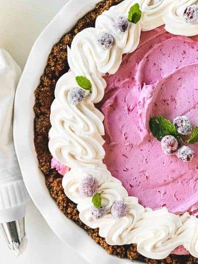 A cranberry mousse pie topped with whipped cream and frosted cranberries.