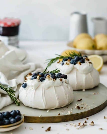 Two mini pavlova nests topped with whipped cream, fresh blueberries, and almonds.